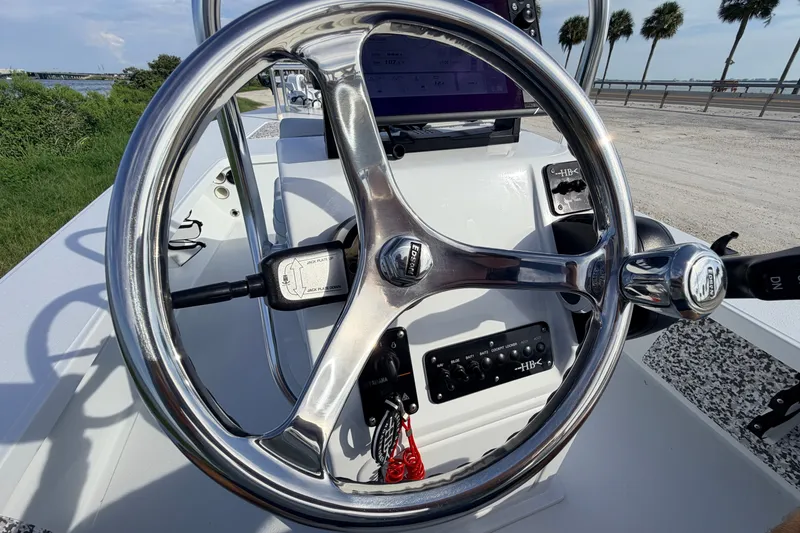 Slide: The Image of 2021 Hell's Bay Marathon boat steering wheel with control panel, near waterfront and palm trees. - 57