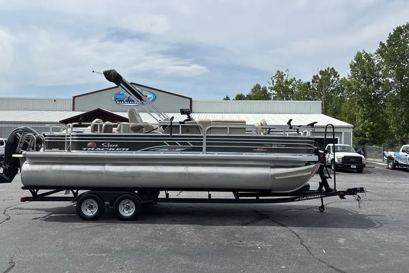 The Image of 2027 Sun Tracker Fishin' Barge 22 XP3 pontoon boat on trailer, parked outdoors. - 0
