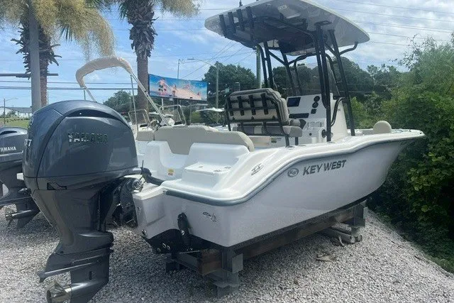 Slide: The Image of 2026 Key West 219 FS boat with Yamaha engine, parked on gravel under palm trees. - 1