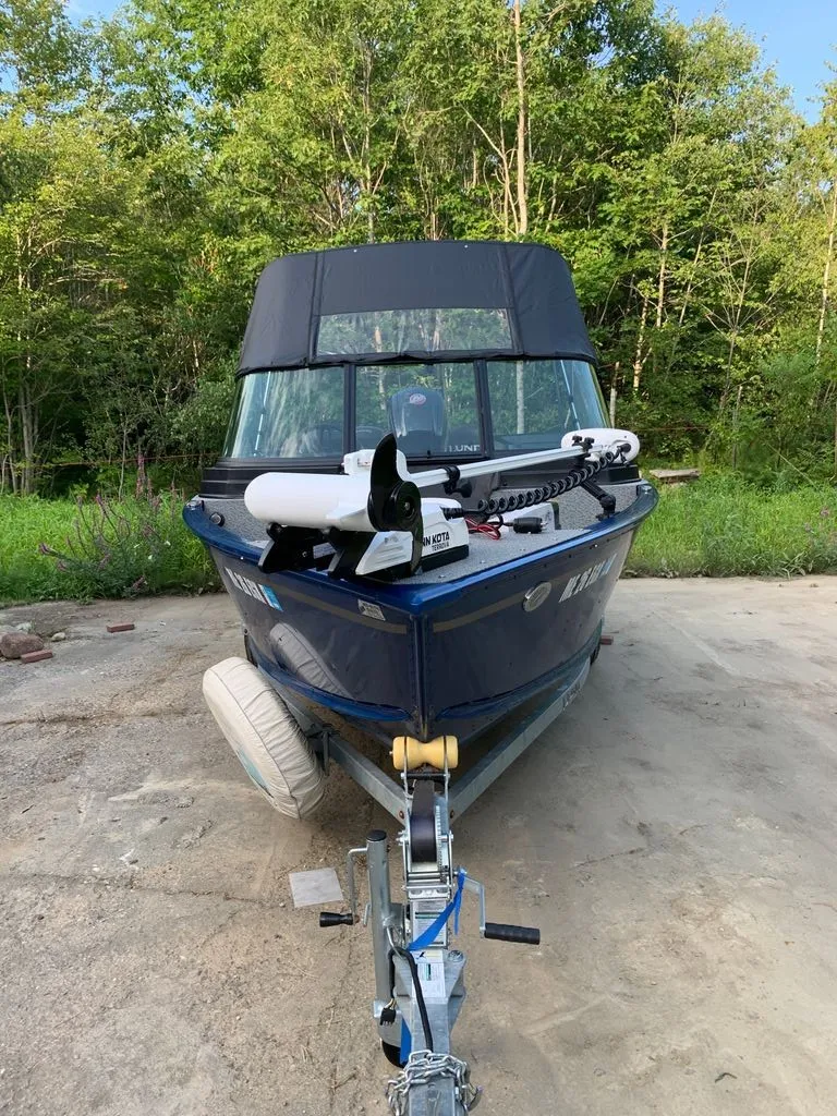 Slide: The Image of A 2024 Lund 1775 Adventure Sport boat on a trailer, surrounded by trees. - 19
