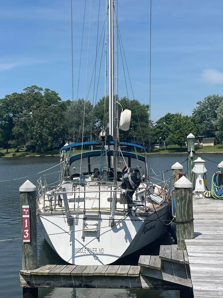 Slide: The Image of A 1985 Catalina Morgan 43 docked at a serene pier. Trees are visible in the background. - 2