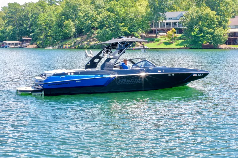Slide: The Image of A 2020 Malibu Wakesetter 24 MXZ on a calm lake, surrounded by trees. - 3