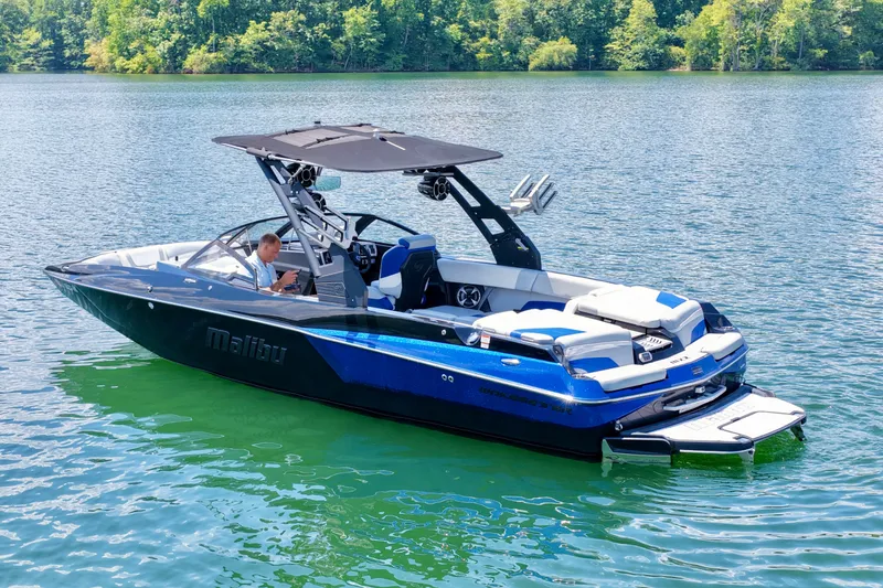 Slide: The Image of 2020 Malibu Wakesetter 24 MXZ boat on a serene lake with lush green surroundings. - 6