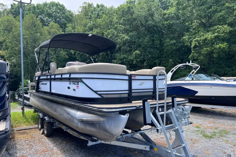 Slide: The Image of 2024 Starcraft SLS 3 pontoon boat on trailer, parked outdoors with lush trees in background. - 2