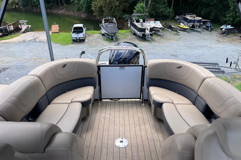 Slide: The Image of 2024 Starcraft SLS 3 pontoon boat interior with plush seating, docked near a lake. - 8