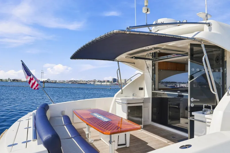 Slide: The Image of 2009 Riviera 4700 Sport Yacht with American flag, docked by the water, featuring outdoor seating. - 6