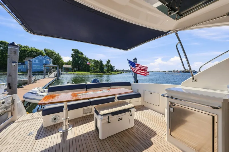 Slide: The Image of 2009 Riviera 4700 Sport Yacht deck with seating, table, and American flag by the water. - 8