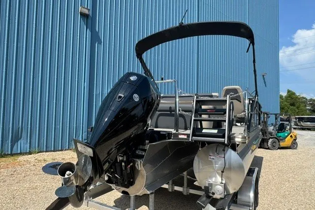 Slide: The Image of 2027 Barletta Aria 24UC pontoon boat with outboard motor, parked near a blue building. - 4