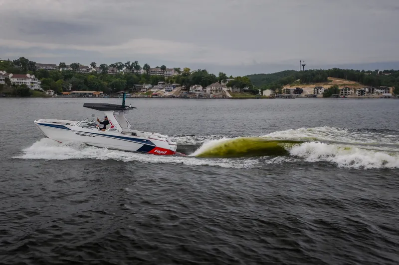 Slide: The Image of 2027 Tige Ultré 25ZX boat cruising on a scenic lake with shoreline houses. - 6