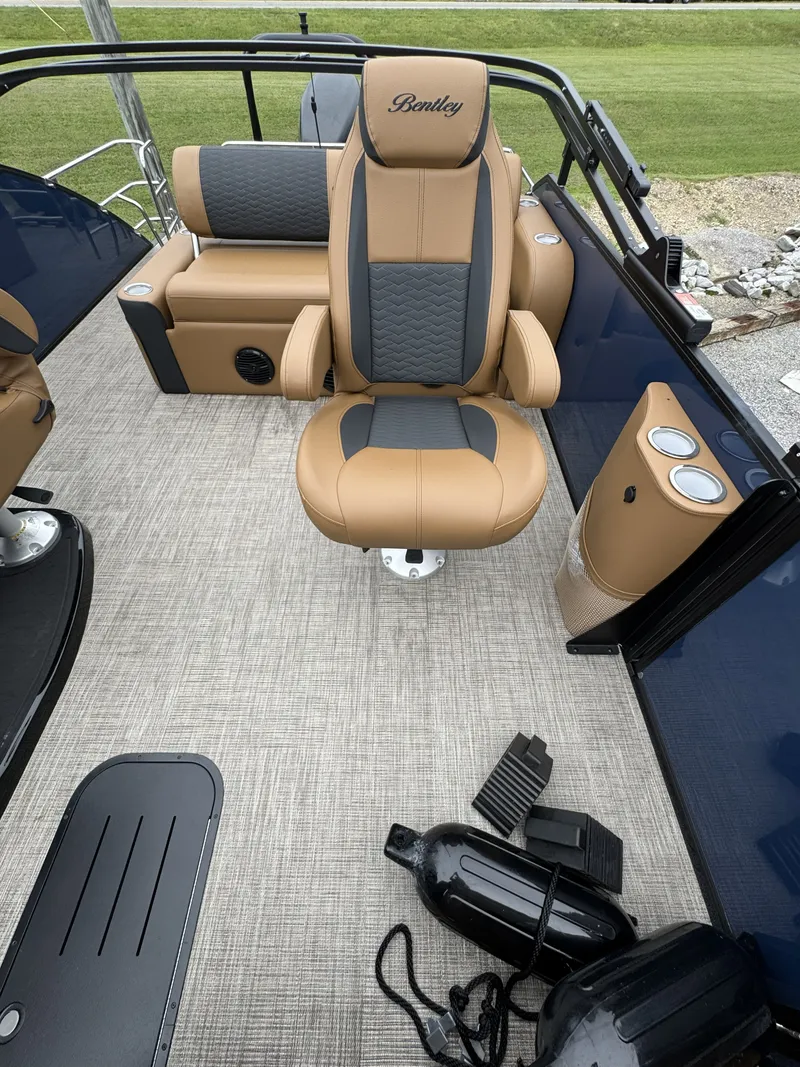 Slide: The Image of The image shows the interior of a 2026 Bentley Pontoons Elite 223 SwingBack DC. There's a cushioned captain's chair in brown and gray, surrounded by blue walls and textured flooring. - 12