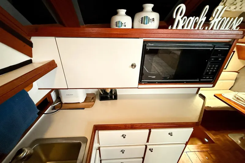 Slide: The Image of 1989 Tiara Yachts 3600 Convertible kitchen with microwave, sink, and "Beach House" decor. - 36