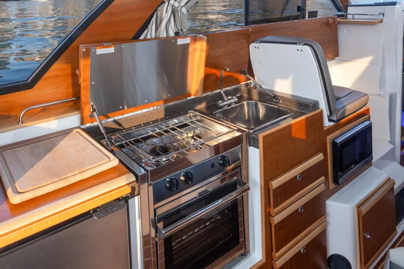 Slide: The Image of 2023 Cutwater C-30 Sedan boat kitchen with stove, sink, and wooden cabinetry. - 30