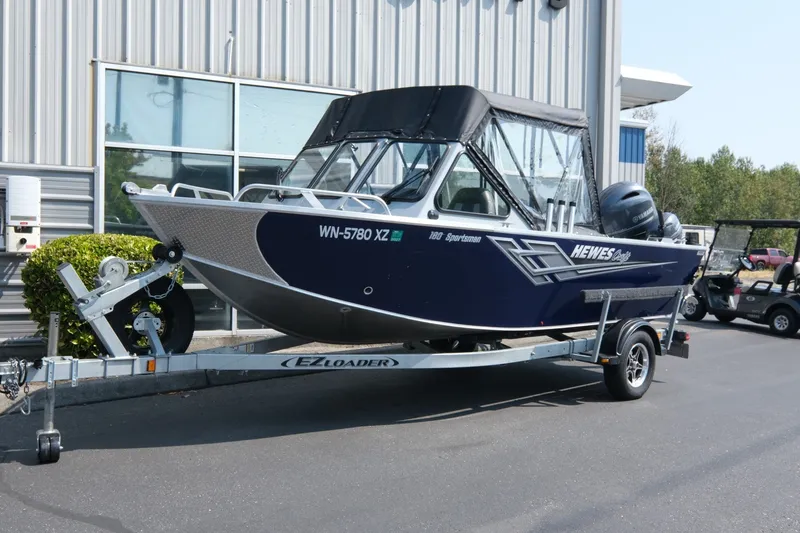 The Image of 2023 Hewescraft 180 Sportsman boat on EZ Loader trailer, parked outside a building. - 1
