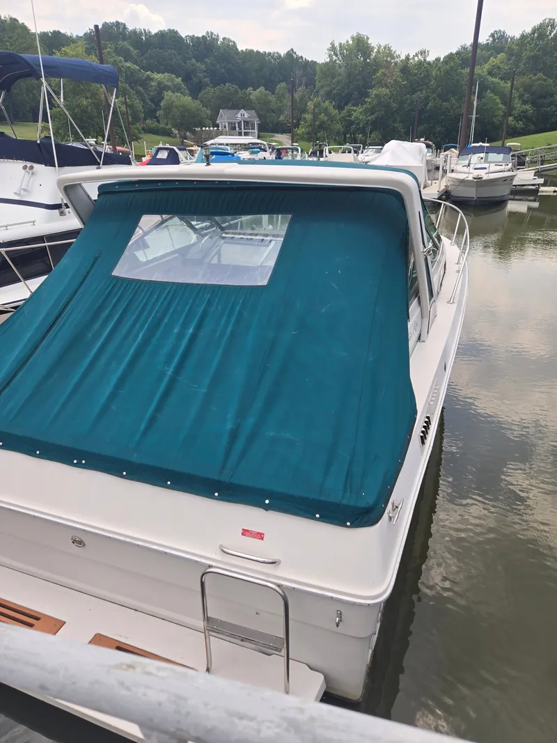 Slide: The Image of A 1987 Sea Ray 300 Weekender with a blue cover, docked in a calm marina. - 3