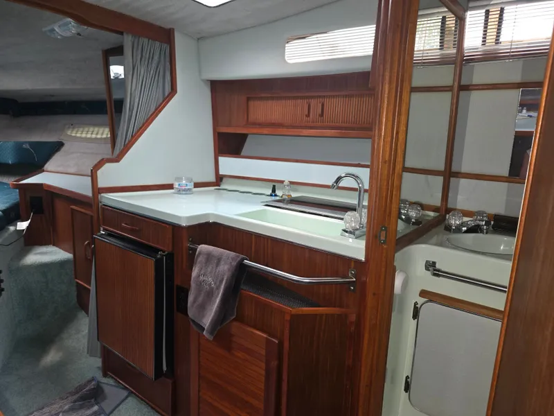 Slide: The Image of The interior of a 1987 Sea Ray 300 Weekender features a compact kitchen with wooden cabinets. - 9