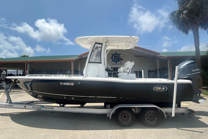 The Image of 2018 Sea Hunt BX25FS boat on trailer, parked outside a marine facility under a clear sky. - 0