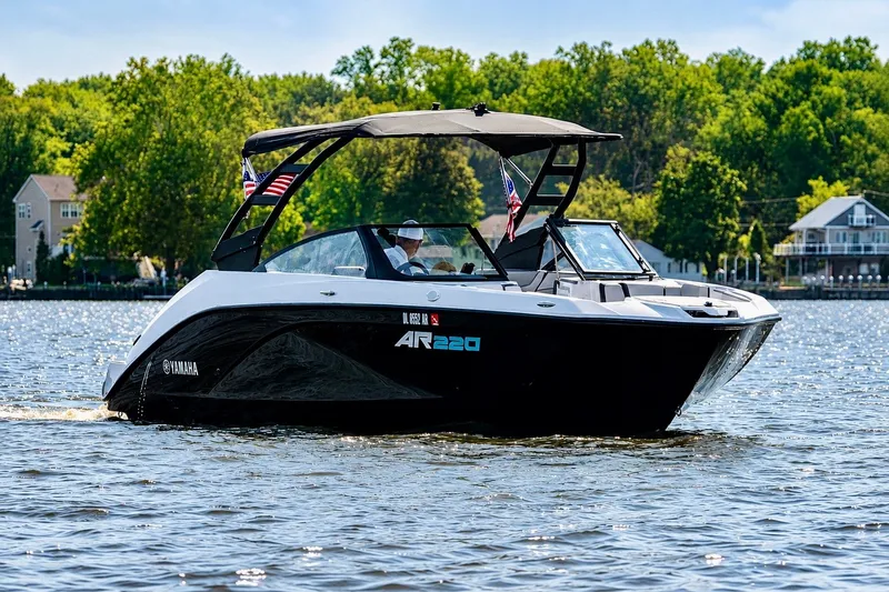 The Image of 2025 Yamaha Boats AR220 cruising on a scenic lake with lush green trees. - 0