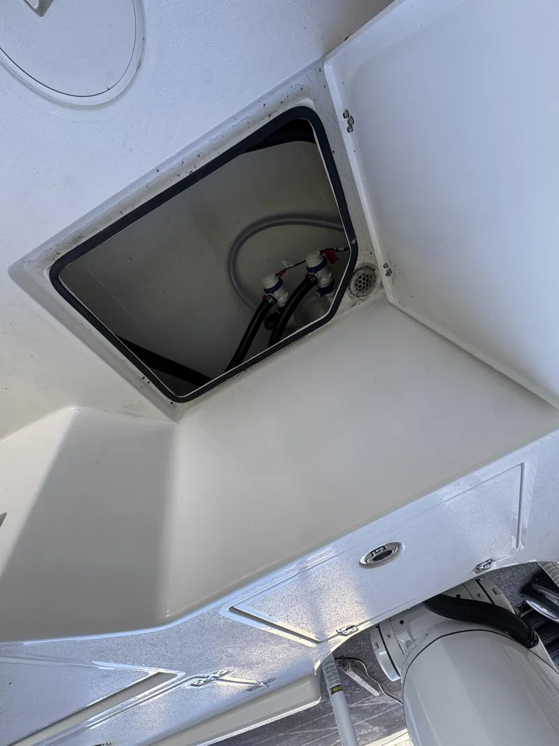 Slide: The Image of An open storage compartment on a 2027 Pathfinder 2500 Tournament boat, with visible hoses. - 48