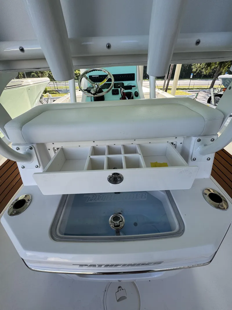 Slide: The Image of The image shows the cockpit of a 2027 Pathfinder 2500 Tournament boat. There's a white seat cushion with a drawer underneath containing compartments. The helm with instruments is visible in the background. - 50