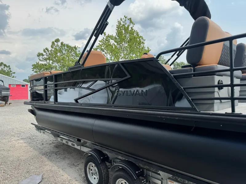 Slide: The Image of A 2026 Sylvan L3 RLZ pontoon boat on a trailer. It features black sides and brown seats. - 23