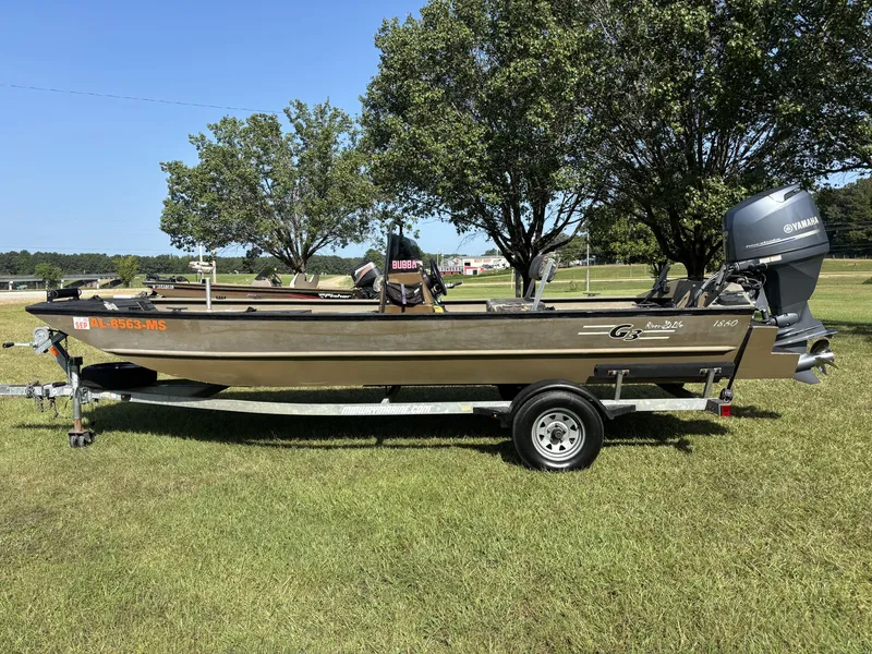 The Image of A 2013 G3 1860 CCT boat on a trailer in a grassy area, surrounded by trees. - 1
