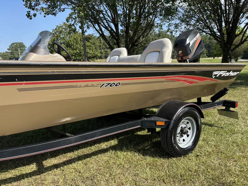 Slide: The Image of A 2006 Fisher Boats 1700 on a trailer, set on grass, surrounded by trees. - 11
