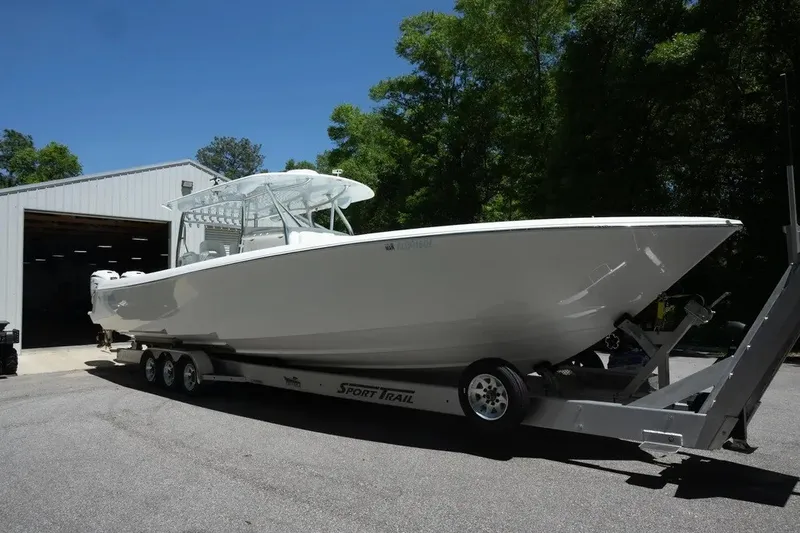 The Image of 2023 Contender 44 ST boat on trailer outside a garage, surrounded by trees. - 1