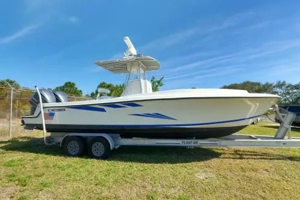 The Image of 1999 Contender 28 Sport boat on trailer, parked on grass under clear blue sky. - 1