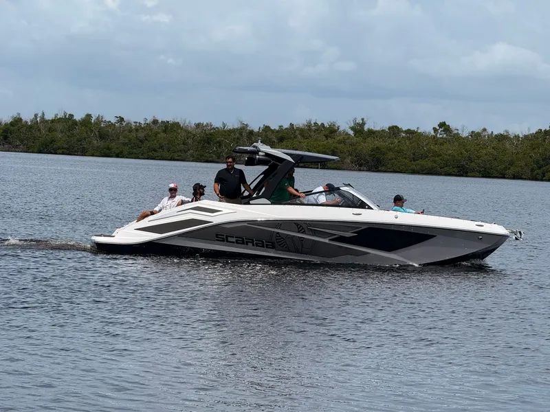 Slide: The Image of A 2026 Scarab 285 LX boat cruising on calm water with several people on board. - 5