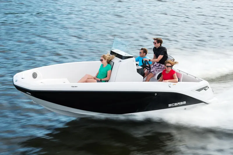 Slide: The Image of A 2019 Scarab 195 Open G boat speeds across the water with four people on board. - 2