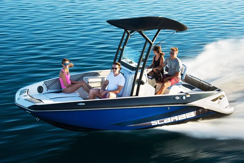 Slide: The Image of A 2019 Scarab 195 Open ID boat speeds across calm water. Four people are seated onboard. - 6