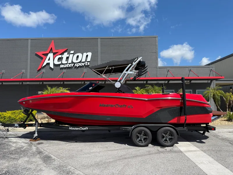 The Image of A red 2022 MasterCraft NXT24 boat on a trailer in front of a water sports store. - 1