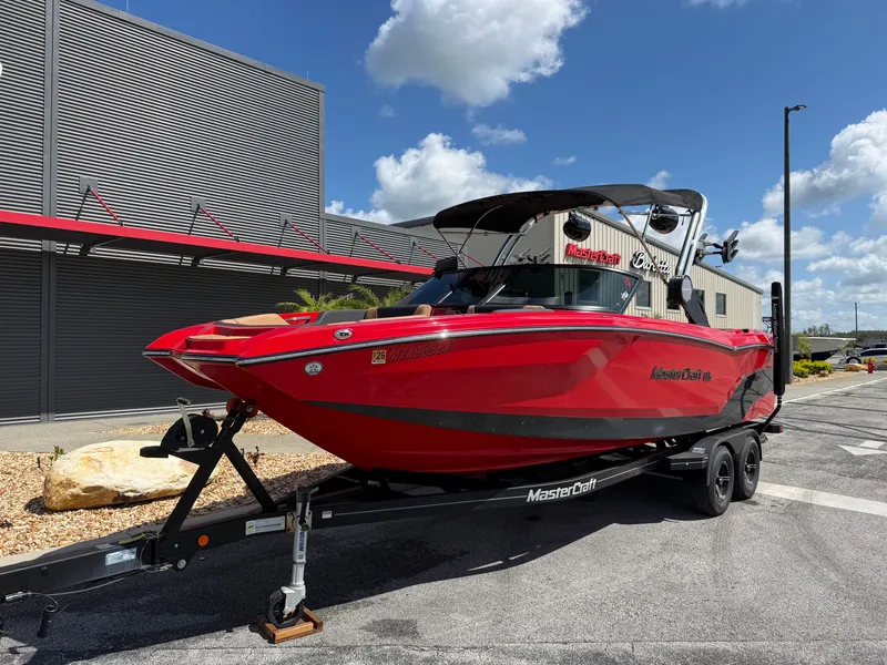 Slide: The Image of A red 2022 MasterCraft NXT24 boat on a trailer in front of a modern building. - 2