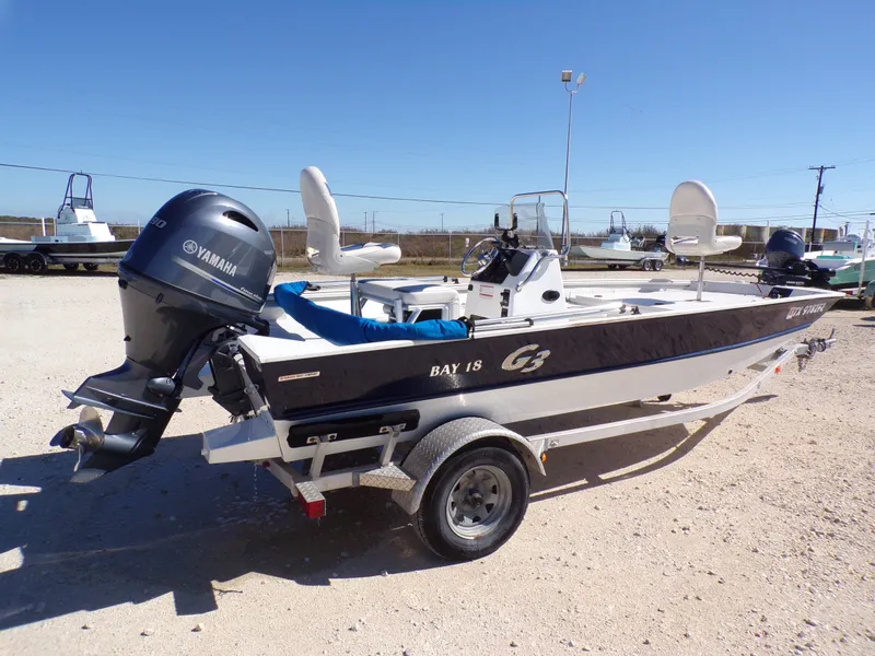 The Image of A 2018 G3 Bay 18 boat on a trailer with a Yamaha outboard motor, on a gravel lot. - 1