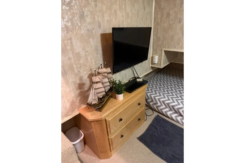 Slide: The Image of Houseboat interior with TV, wooden dresser, model ship, and chevron-patterned bedding. - 29
