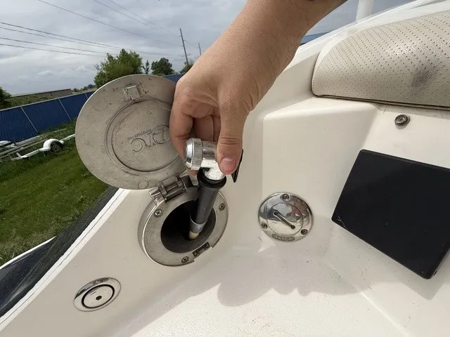 Slide: The Image of A hand holds a fuel cap on a white boat. The background shows a fence and trees. - 29