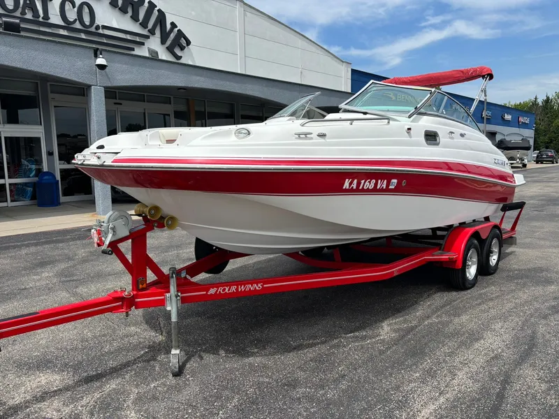 Slide: The Image of A white and red Four Winns 214 Fun Ship boat from 2003 on a trailer in front of a building. - 2