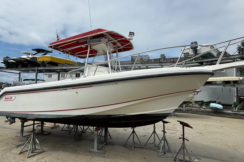 The Image of 1998 Boston Whaler 23 Outrage boat on stands, featuring a red canopy and sleek design. - 0