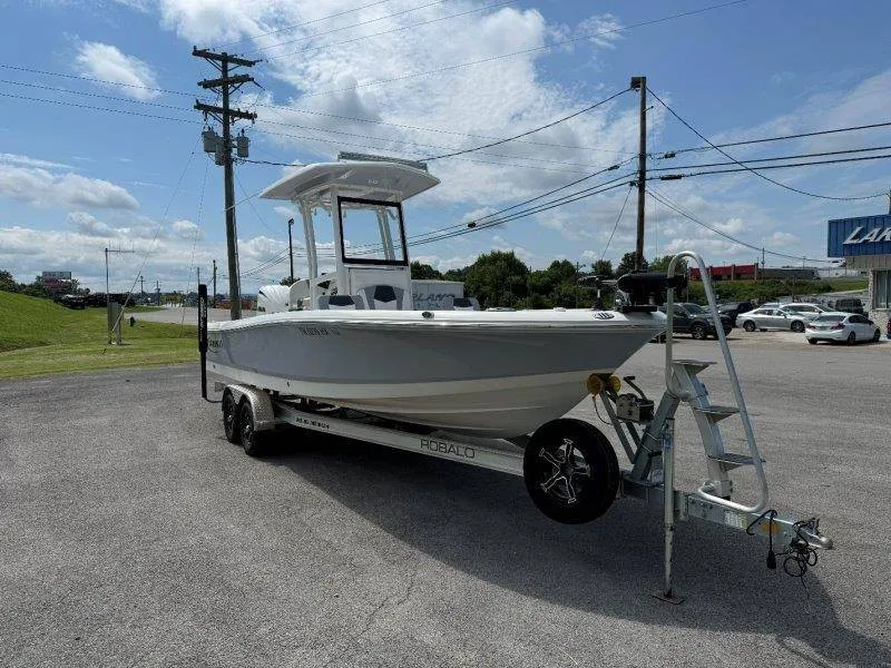 Slide: The Image of A 2023 Robalo 246 Cayman on a trailer in a parking lot, surrounded by power lines. - 8