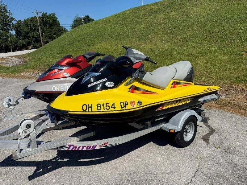 The Image of Two Sea-Doo jet skis on a trailer, one yellow and one red, in a parking area. - 1