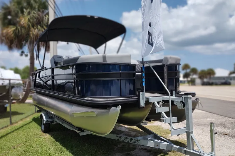 The Image of 2027 Sylvan X1 ULZ pontoon boat on trailer, parked outdoors under a cloudy sky. - 0