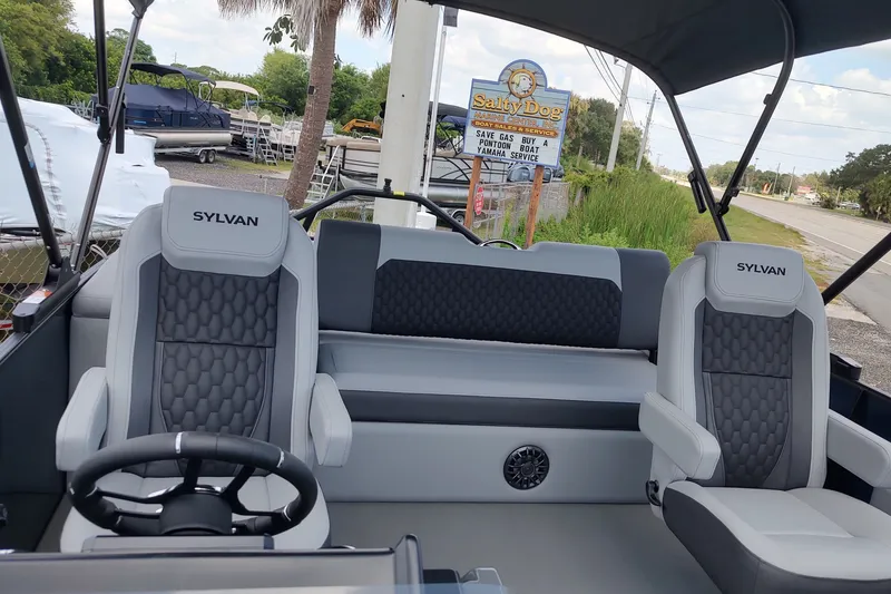 Slide: The Image of 2027 Sylvan X1 ULZ boat interior with stylish seating and steering wheel, parked near Salty Dog sign. - 2