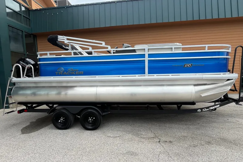 The Image of 2027 Sun Tracker Fishin' Barge 20 DLX pontoon boat on trailer, blue and silver design. - 0
