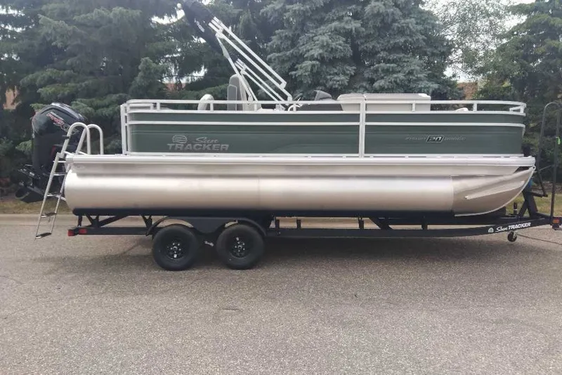 The Image of 2027 Sun Tracker Fishin' Barge 20 DLX pontoon boat on trailer, parked outdoors. - 0