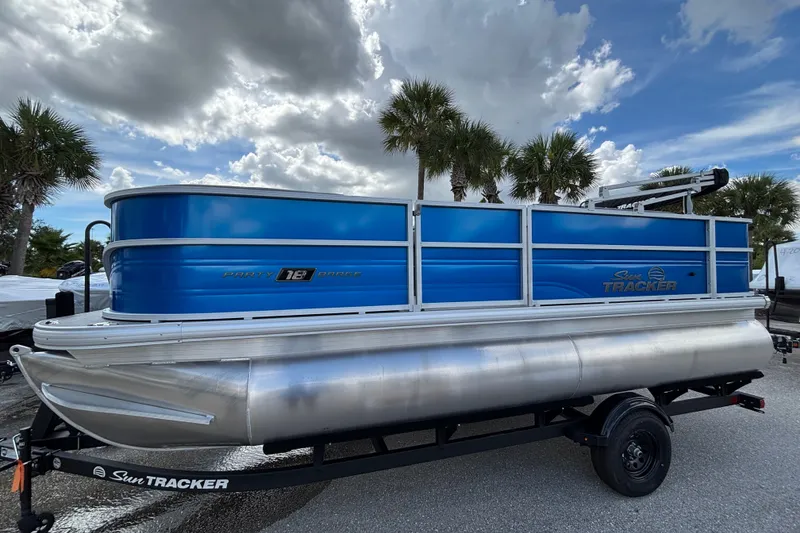 The Image of 2027 Sun Tracker Party Barge 18 DLX pontoon boat on trailer, under cloudy sky. - 0