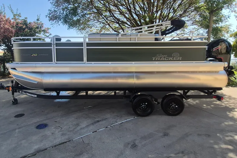 The Image of 2027 Sun Tracker Fishin' Barge 20 DLX pontoon boat on trailer, parked outdoors. - 0