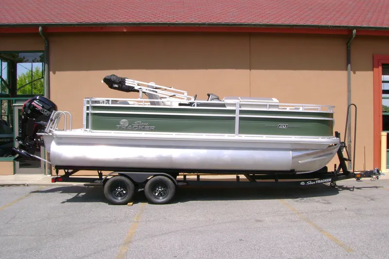 The Image of 2027 Sun Tracker Fishin' Barge 20 DLX pontoon boat on trailer, parked outdoors. - 0