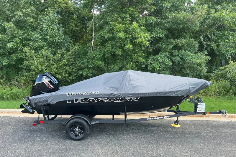 Slide: The Image of 2027 Tracker Pro Guide V-16 SC boat with cover on trailer, parked by trees. - 14