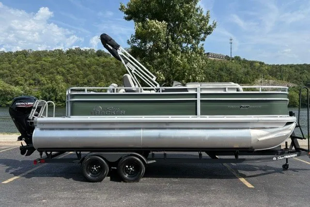 The Image of 2027 Sun Tracker Fishin' Barge 20 DLX pontoon boat on trailer, parked near a lake. - 0