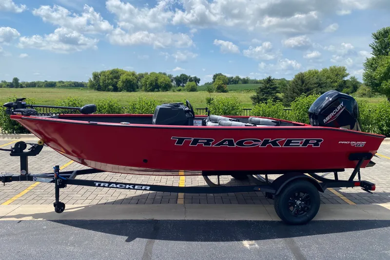The Image of 2027 Tracker Pro Guide V-16 SC boat on trailer, red exterior, parked outdoors. - 0